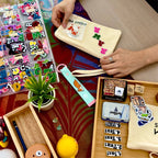 A hands-on personalization session at The Goodayy studio showing a customer choosing colorful iron-on letters and cat patches to decorate a cream canvas pouch.