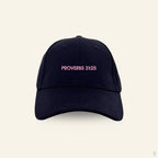 Black baseball cap with pink 'Proverbs 31:25' text on a beige background