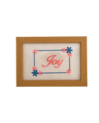 Medium-toned wood frame with pink script reading "Joy" surrounded by an embroidered blue and pink floral border.