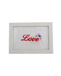 Light wood frame featuring red cursive embroidered text reading "Love" and a small floral detail on cream canvas.