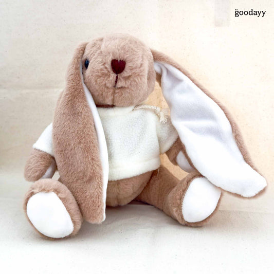 Plush toy rabbit with a white shirt on a beige background, branded ' the goodayy'.