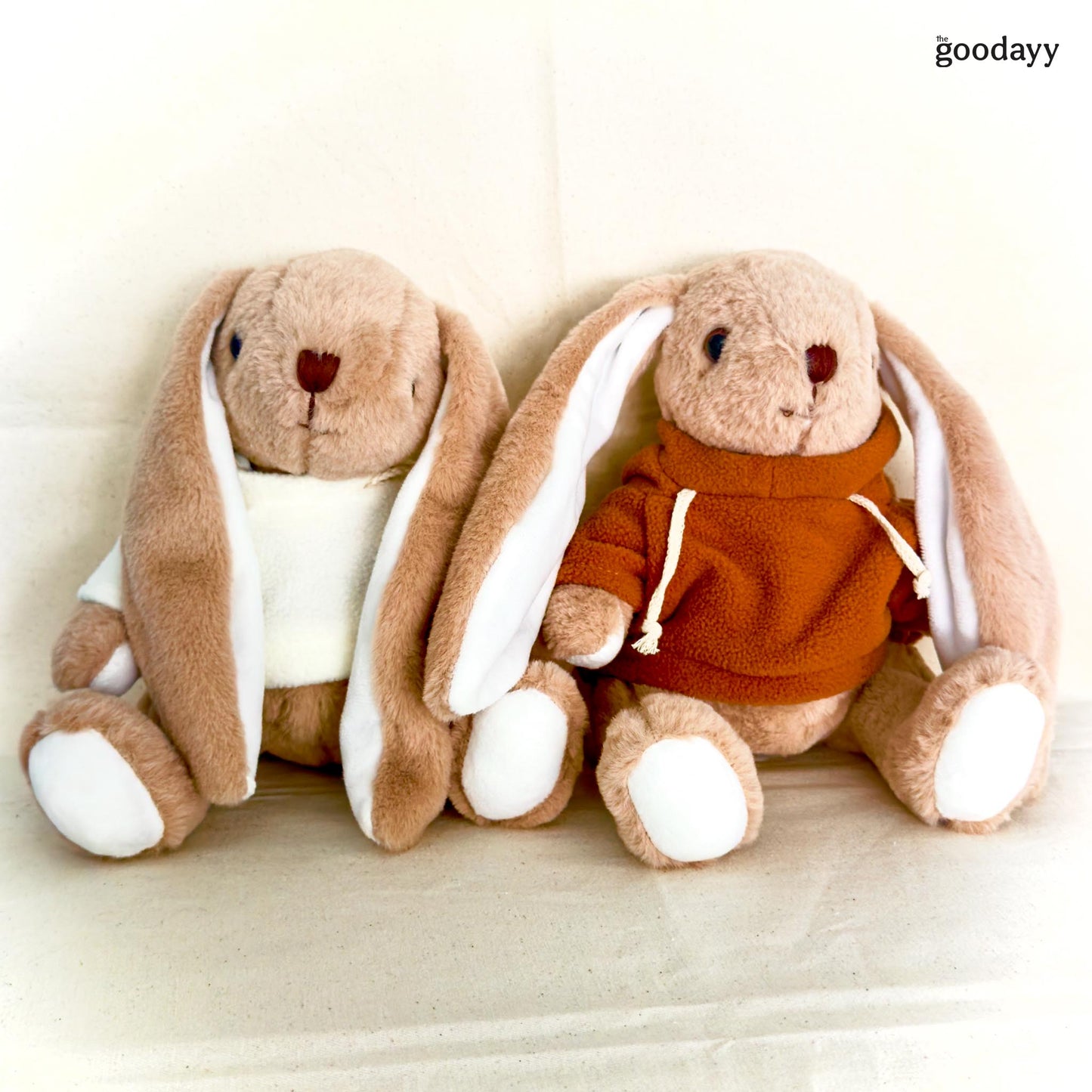 Two plush bunny toys, one in a white shirt and the other in an orange hoodie, on a light background.
