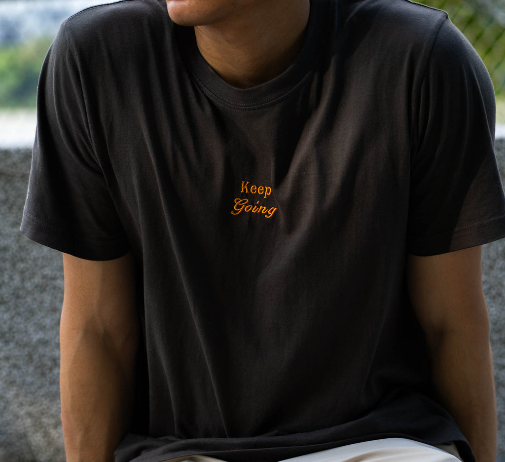 Image of model wearing  "keep going" embroidered on a 200gsm cotton tee that is available in 3 colours and available in 4 sizes, S M L XL and 2XL.
