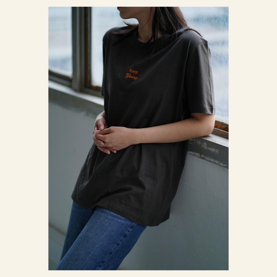 Image of model wearing  "keep going" embroidered on a 200gsm cotton tee that is available in 3 colours and available in 4 sizes, S M L XL and 2XL.