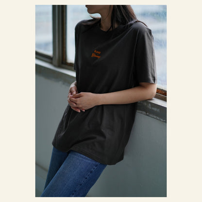 Image of model wearing  "keep going" embroidered on a 200gsm cotton tee that is available in 3 colours and available in 4 sizes, S M L XL and 2XL.