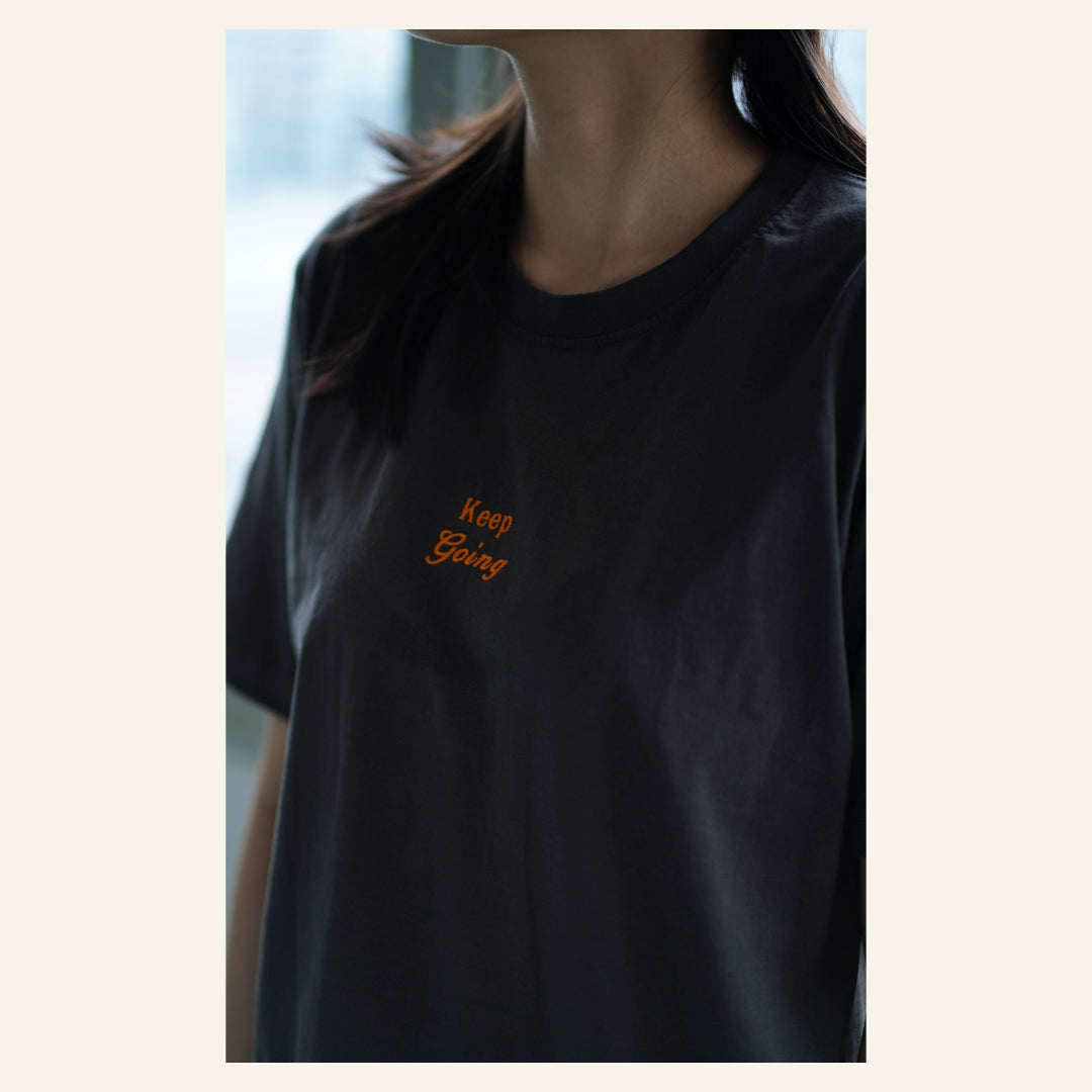 Image of model wearing  "keep going" embroidered on a 200gsm cotton tee that is available in 3 colours and available in 4 sizes, S M L XL and 2XL.