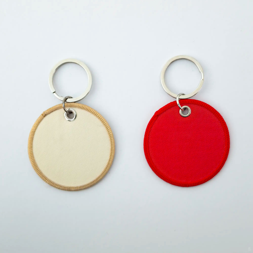 Two round keychains, one beige and one red, on a light gray background.