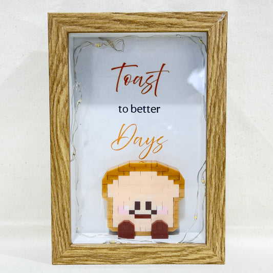 Decorative frame with toast-shaped lego and 'Toast to better days' text in the frame.