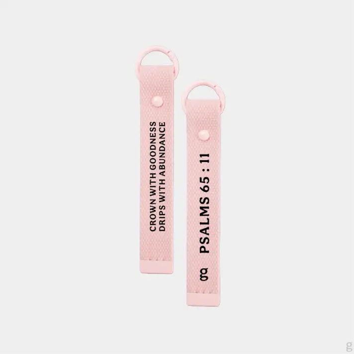The Goodayy pink keychain strap tag with "crown with goodness, drips with abundance" and "Psalms 65 : 11" printed on the flip side