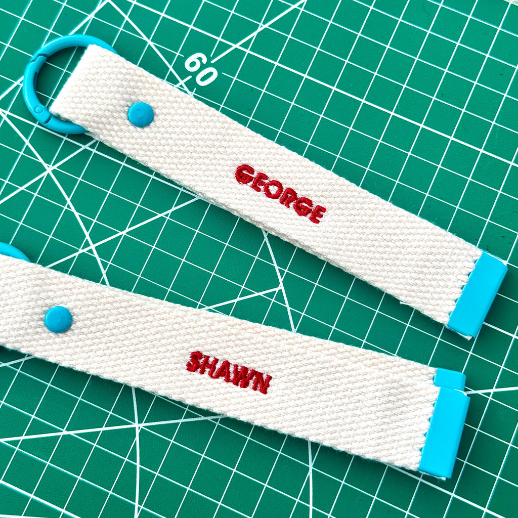 Two white personalize embroidery keychain strap with client's name "Geogre" and "Shawn" .