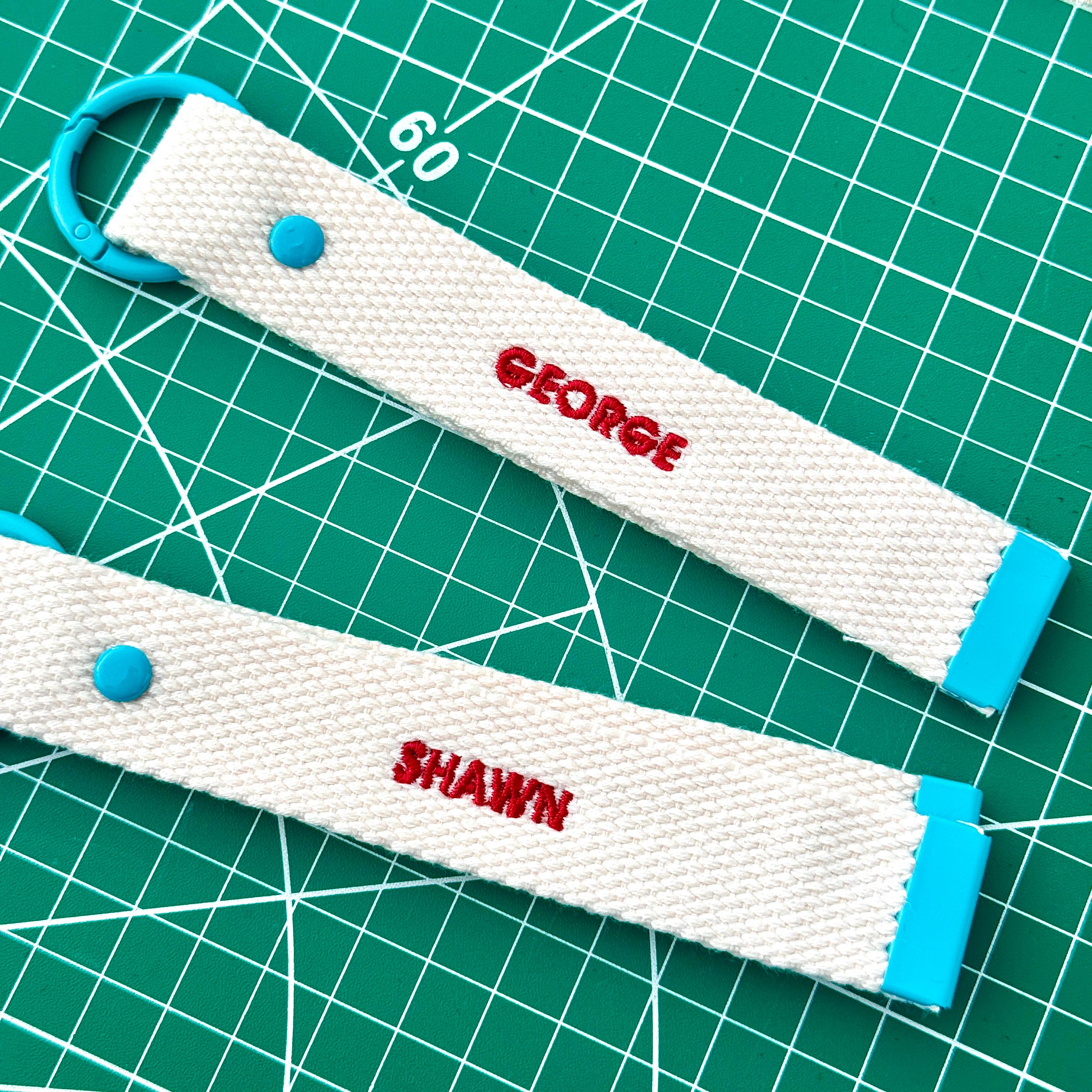 Two white personalize embroidery keychain strap with client's name "Geogre" and "Shawn" .